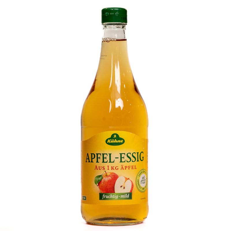 Bottled Kuhne Apple Cider Vinegar for health, with a clear label and a splash of vinegar in a glass on a kitchen counter